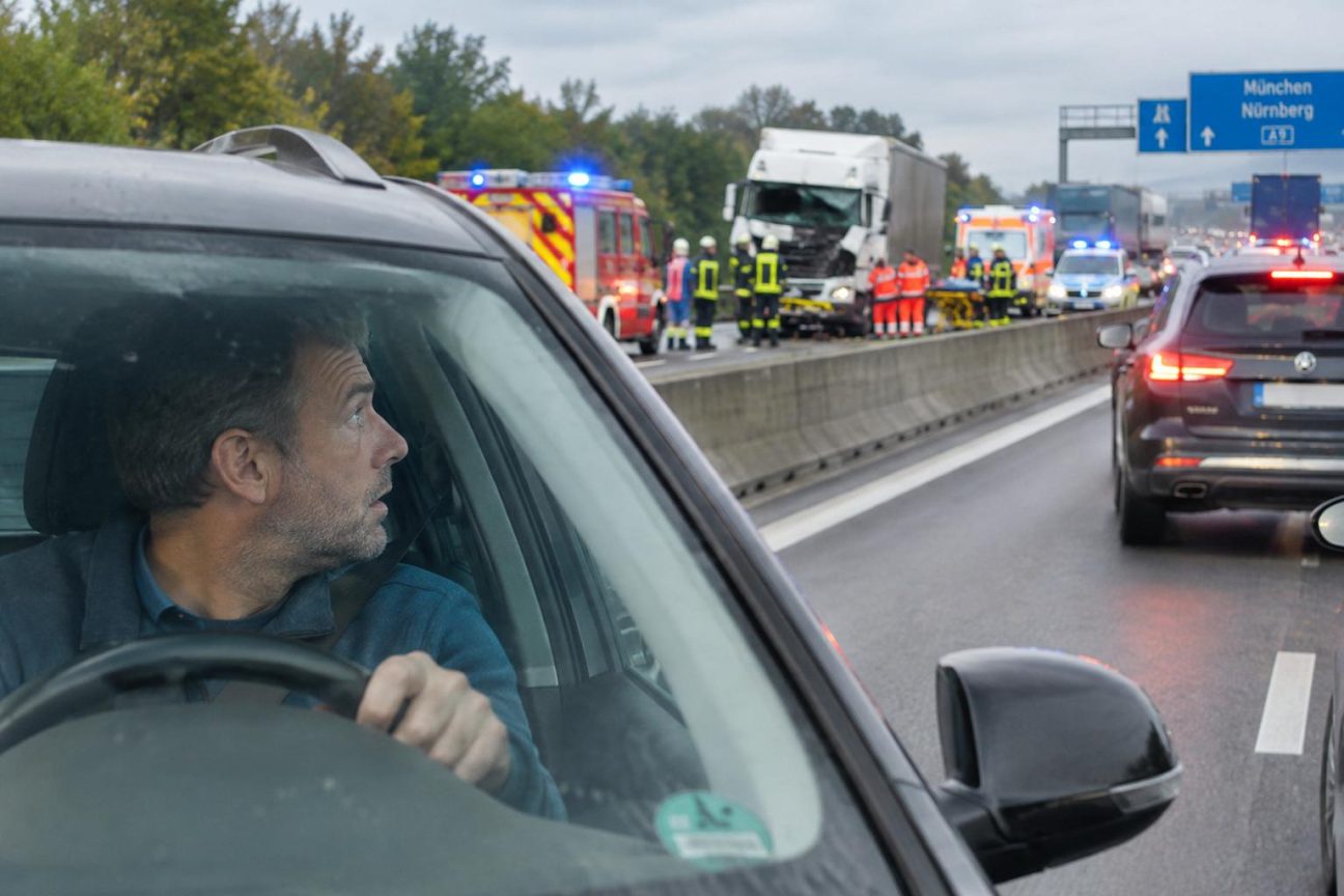 Autoroute congestionnée avec gyrophares de secours visibles, conducteurs ralentissant pour observer un accident sur l'accotement.