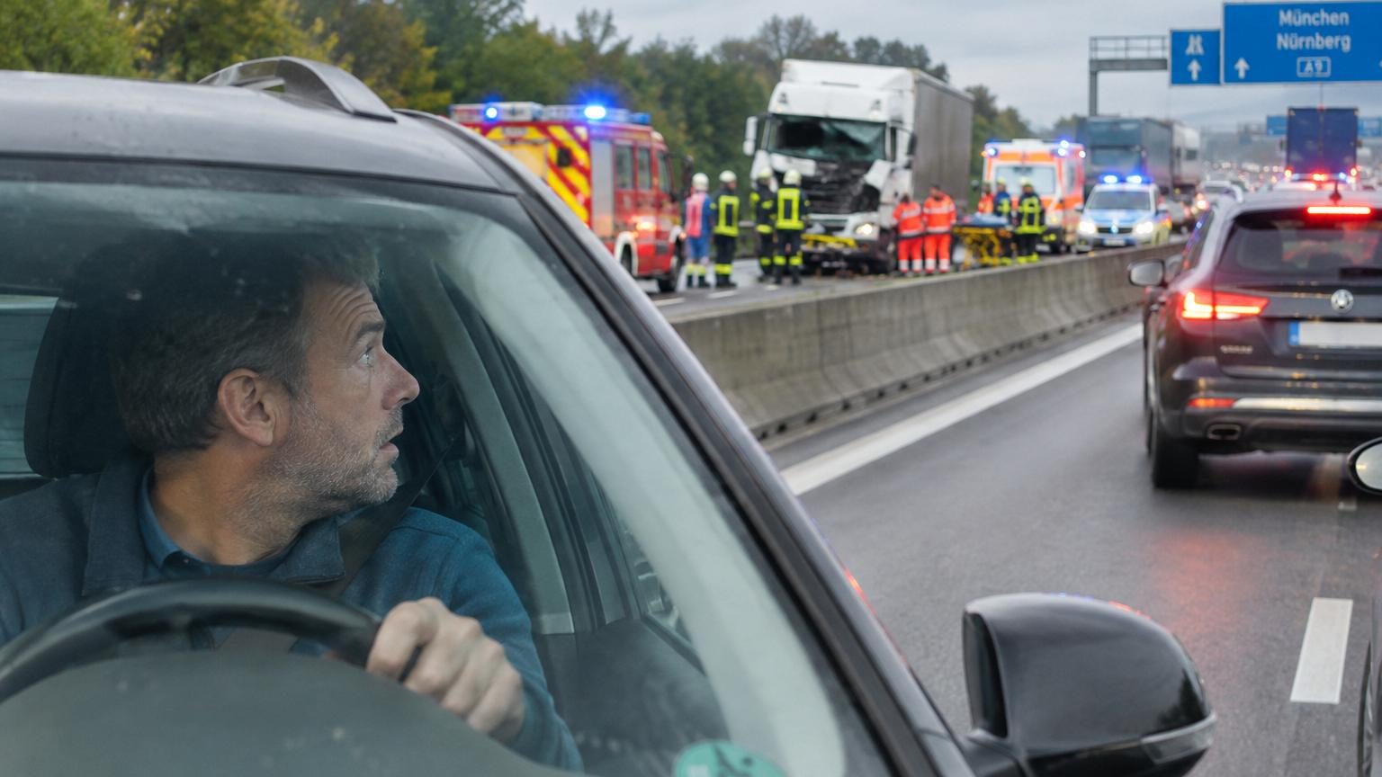 Autoroute congestionnée avec gyrophares de secours visibles, conducteurs ralentissant pour observer un accident sur l'accotement.