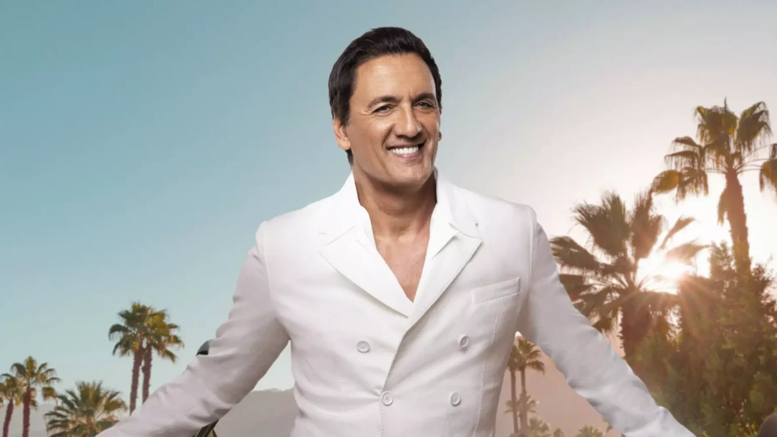 Dany Brillant en tenue élégante rétro sur scène, micro en main, souriant face à un public nombreux et attentif, incarnant le moment de sa première partie décisive.