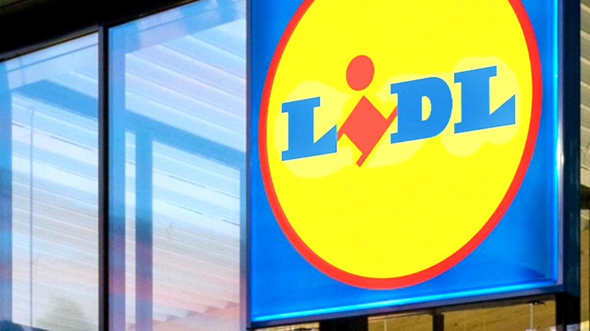 Scène matinale dans une file d'attente Lidl, une cliente montrant sur son téléphone la capture d'écran du nettoyeur Silvercrest 3-en-1, entourée d'autres clients et de chariots.