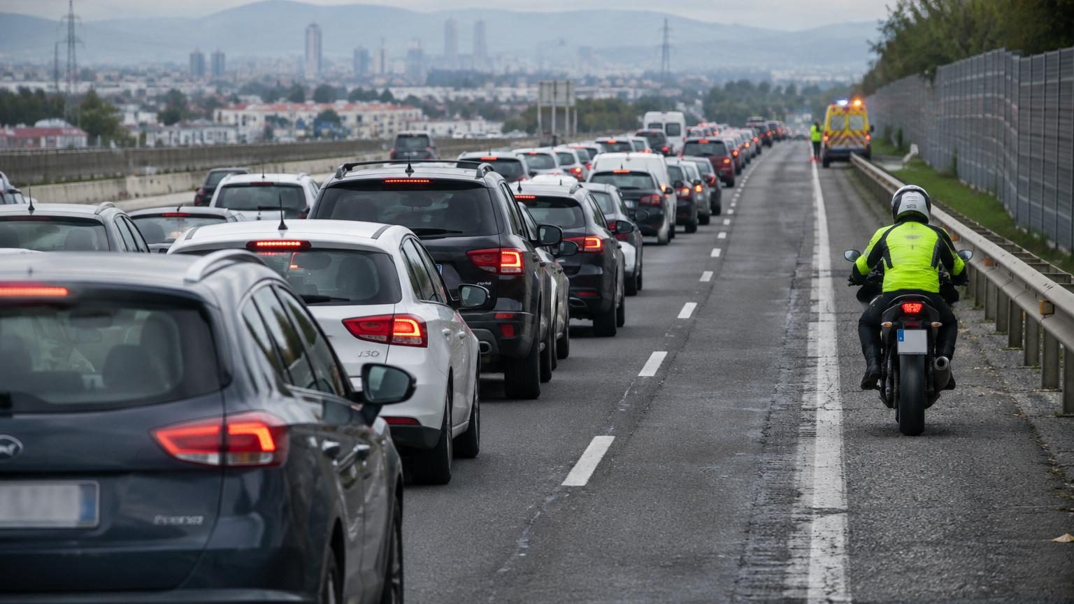 Moto circulant seule sur la bande d'arrêt d'urgence d'une autoroute espagnole avec signalisation verticale et marquages au sol spécifiques, embouteillage de voitures à l'arrêt sur les voies adjacentes.