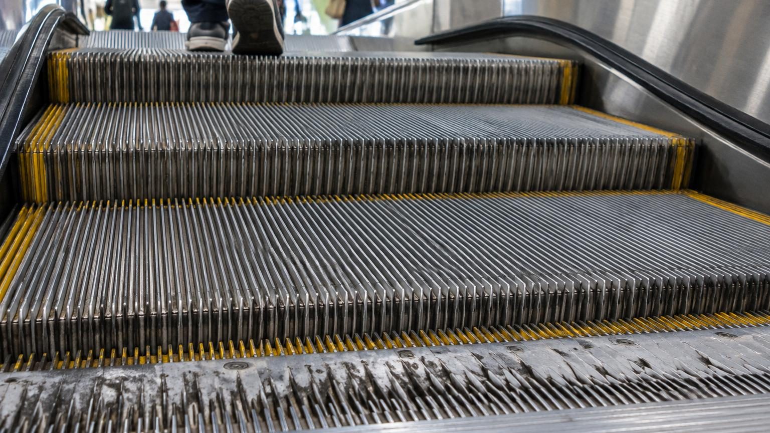 Gros plan sur les rainures dentelées et les dents métalliques d'une marche d'escalator s'emboîtant dans le peigne immobile au sol.