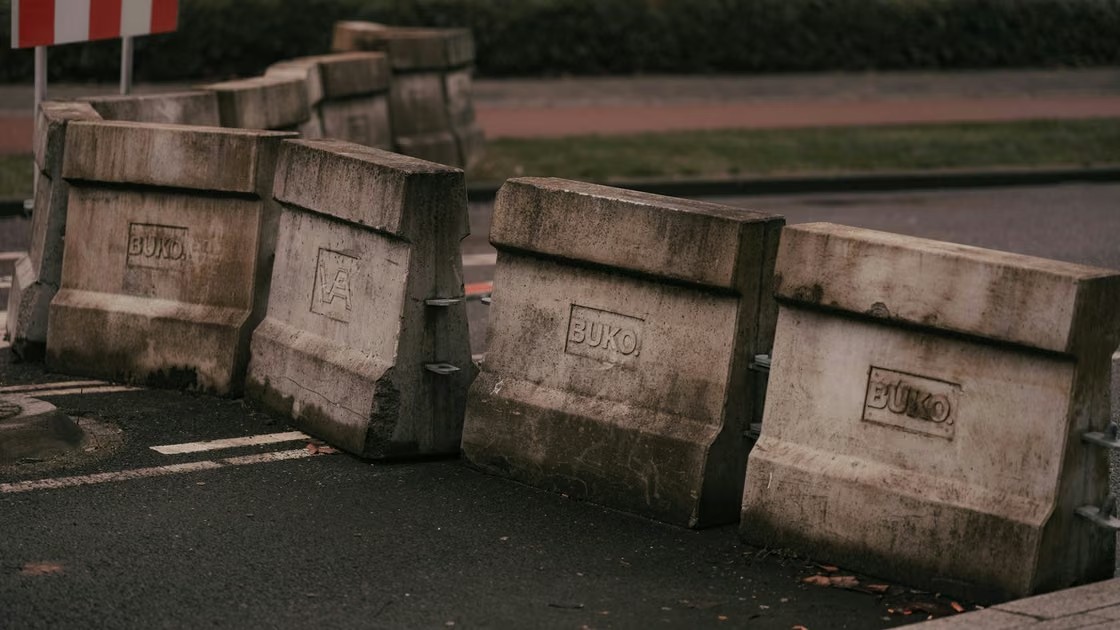 Rangée de blocs de béton posés en travers d'une route ou d'un chemin, bloquant l'accès aux véhicules avec des chicanes mises en place à l'entrée d'une parcelle